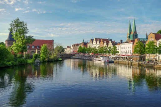 Blick über die Trave auf die Altstadt der Hansestadt Lübeck mit historischen Giebelhäusern, der St.-Marien-Kirche und dem Holstentor im Hintergrund.