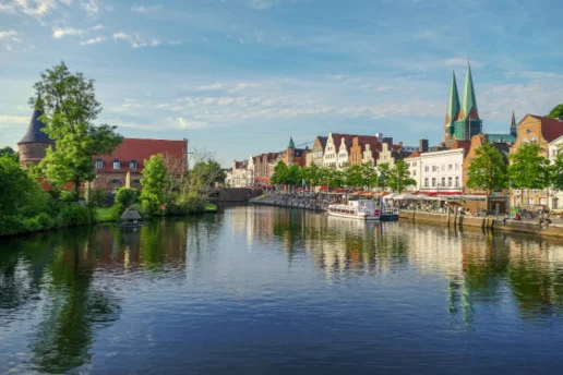 Blick über die Trave auf die Altstadt der Hansestadt Lübeck mit historischen Giebelhäusern, der St.-Marien-Kirche und dem Holstentor im Hintergrund.
