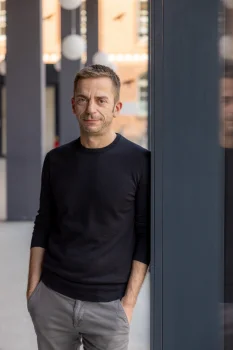 Porträt von Prof. Dr. Clemens Räthel (Nordischer Klang). Er trägt einen schwarzen Pullover, eine graue Hose und lehnt mit den Händen in den Taschen an einer Säule.