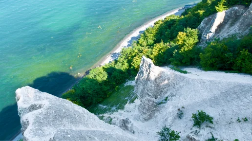 MV-Ostseekooperation - Kreidefelsen auf Rügen Blick von oben auf die markanten weißen Kreidefelsen auf der Insel Rügen. Die steilen Klippen fallen hinab zu einem schmalen Strand am türkisblauen Wasser der Ostsee. Die Hänge sind teilweise mit dichtem, grünem Wald bewachsen.